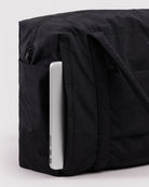 Black nylon laptop bag with exterior pocket holding a silver laptop, showing zippered compartment and carrying handle