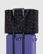 Black duffel bag with red rose print pattern attached to purple rolling suitcase via luggage sleeve