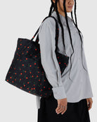 Black tote bag with red rose print pattern carried on shoulder, featuring matching handles and rectangular shape