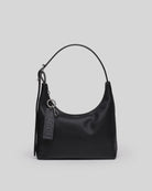 Black leather hobo shoulder bag with single strap and brand tag keychain attachment on grey background