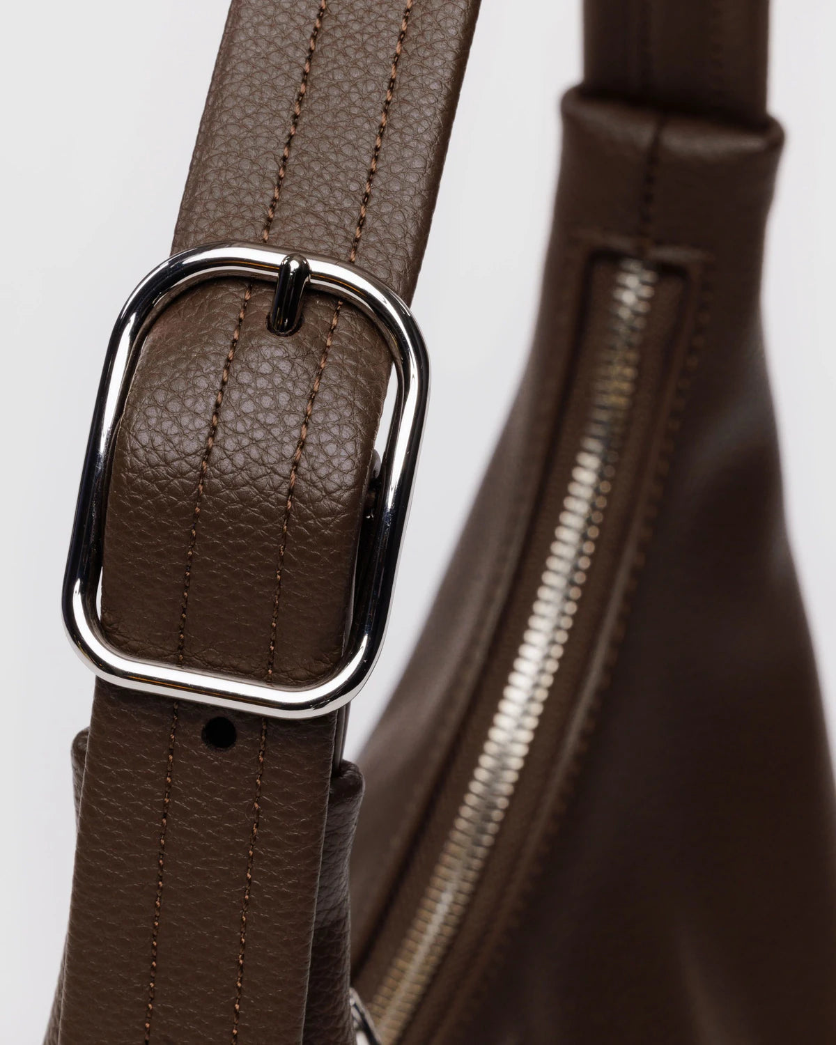 Brown leather bag strap with silver rectangular buckle and zipper detail, featuring contrast stitching and textured grain finish