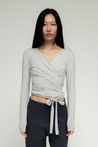 Light gray wrap-style long sleeve top with tie closure at waist, made of soft jersey fabric with ruched detailing