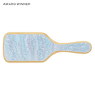 Paddle-shaped hairbrush with blue and purple marbled design, gold trim, and EM JAY branding on handle