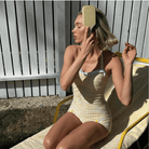 Woman wearing yellow and white gingham check one-piece swimsuit with gray straps relaxing on yellow lounger outdoors