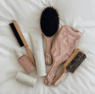 Hair care set with wooden brushes featuring black bristles and marbled pink resin backs, plus cream and serum bottles