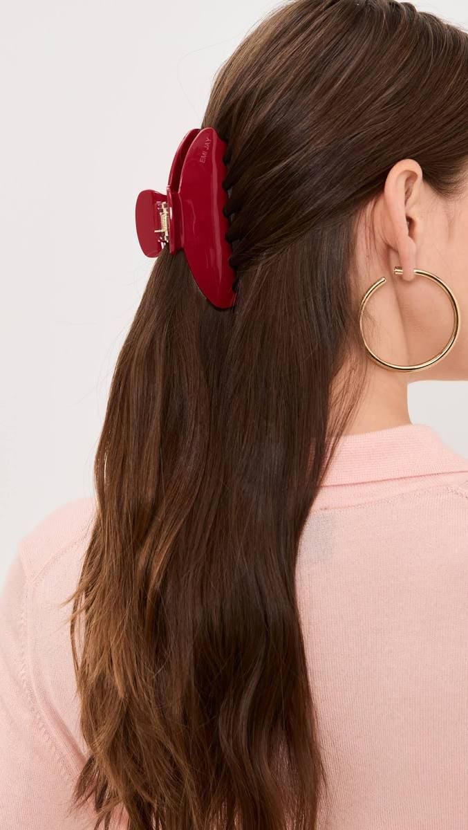 Large red hair claw clip holding back long brown hair, model wearing gold hoop earrings and pink top