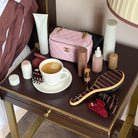Pink quilted makeup bag with gold chain strap and CC logo sitting on vanity table with beauty products and coffee