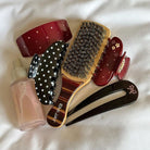 Assorted hair clips and claw clips in burgundy, black, and tortoiseshell with polka dots and star details, plus wooden brush