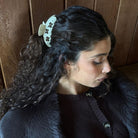 White crochet scrunchie with brown paw print pattern worn in dark curly hair against wooden background