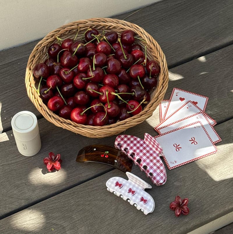 Woven basket of fresh red cherries with pink gingham hair clips, napkins, and cherry-themed accessories on wooden surface