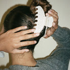 White wide-tooth comb with rounded teeth being used on dark hair, scalp massage and detangling tool