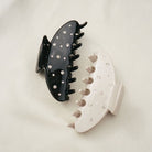 Two decorative hair claw clips with rhinestone embellishments, one in black and one in cream white, displayed on a neutral background