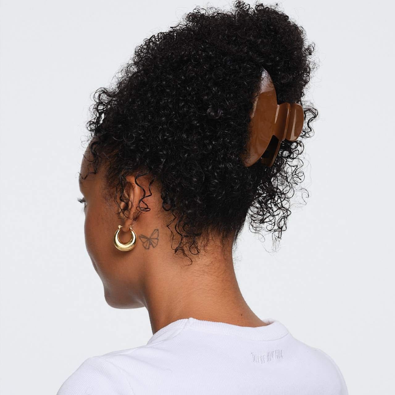 Brown tortoiseshell hair claw clip securing curly black hair in an updo, shown from back view