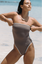 Brown strapless one-piece swimsuit with white contrast piping trim, featuring high-cut legs and bandeau-style top