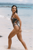One-piece swimsuit in taupe/gray with white piping trim and cutout design, modeled on beach
