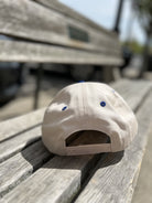 White snapback hat with blue eyelets resting on wooden dock surface with boat in background