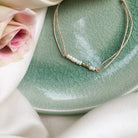 Delicate gold layered necklace with small pearls displayed on green crackle glaze ceramic plate with pink rose
