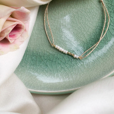 Delicate gold layered necklace with small pearls displayed on green crackle glaze ceramic plate with pink rose