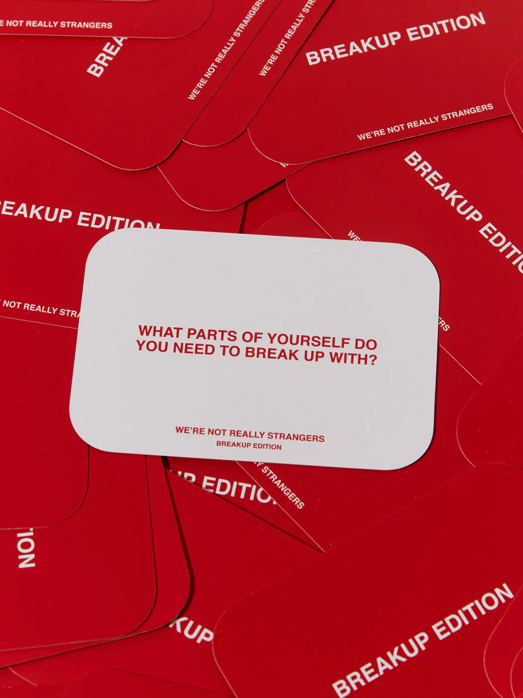 Red card game set titled We're Not Really Strangers Breakup Edition with white card showing introspective question about self-growth
