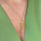 Gold fish skeleton pendant necklace on delicate silver chain worn against green fabric background