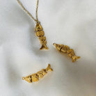 Gold articulated fish pendant necklace with matching charms featuring textured scales and tail fins on white fabric