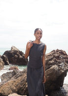 Black sleeveless linen midi dress with tie straps, worn by model standing on rocky coastline