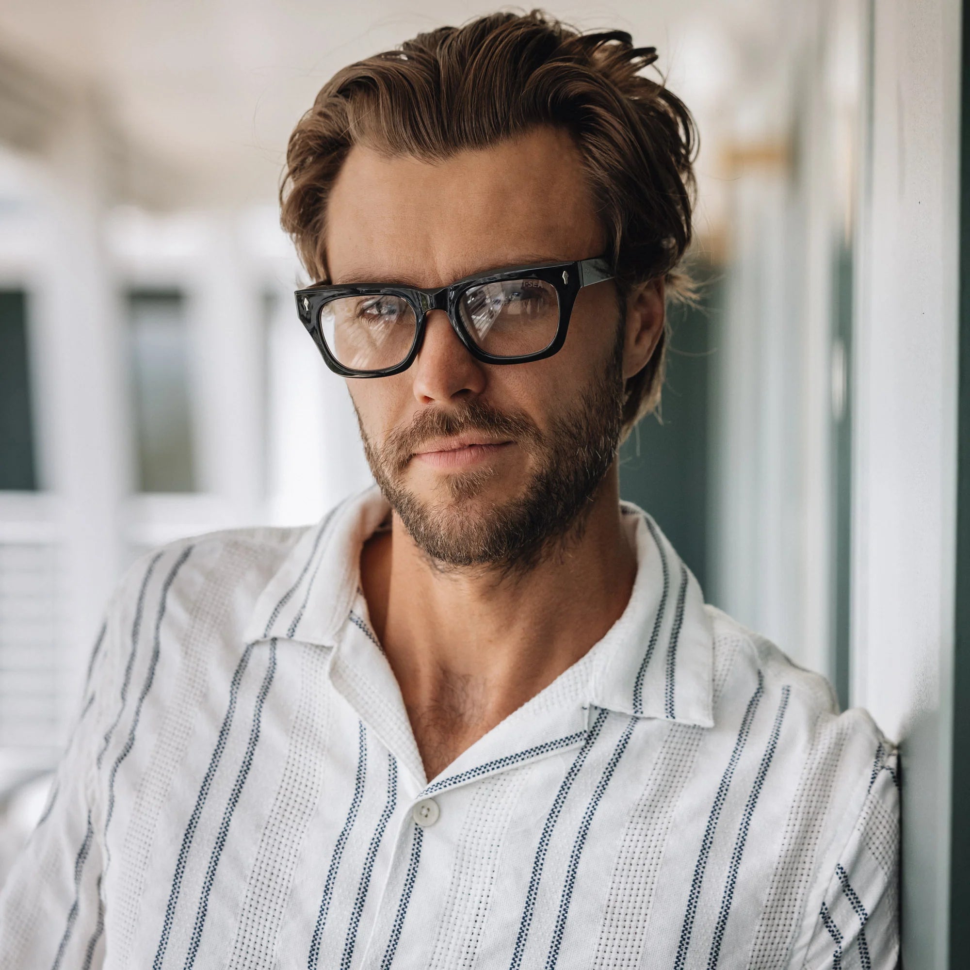 Man wearing glasses and a white shirt with a blurred indoor background