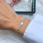 Delicate turquoise beaded bracelet with silver elephant charm on wrist against white fabric background