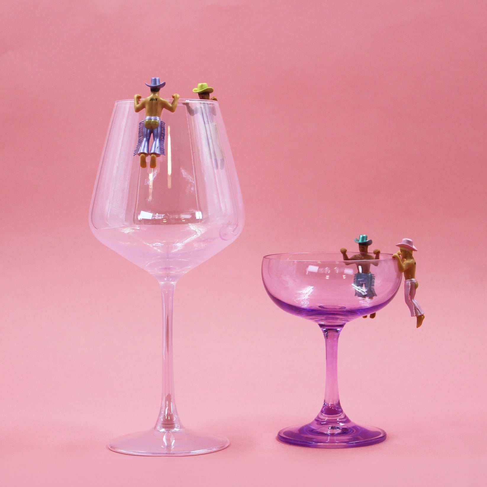 Two glasses, one large and one small, with miniature figures on a pink background