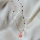 Delicate silver chain necklace with pink gemstone beads and coral pink seashell pendant on white satin fabric