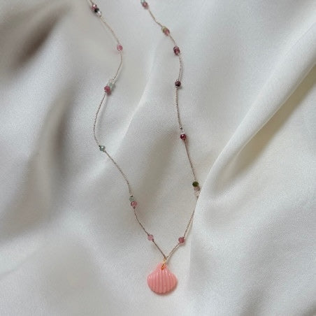 Delicate silver chain necklace with pink gemstone beads and coral pink seashell pendant on white satin fabric