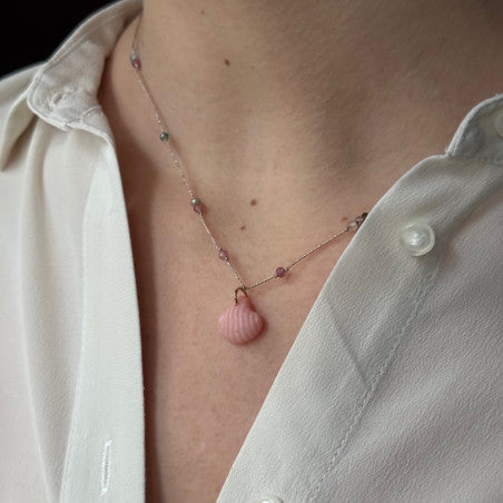 Delicate rose gold necklace with pink shell pendant and small gemstone beads worn on person in white shirt