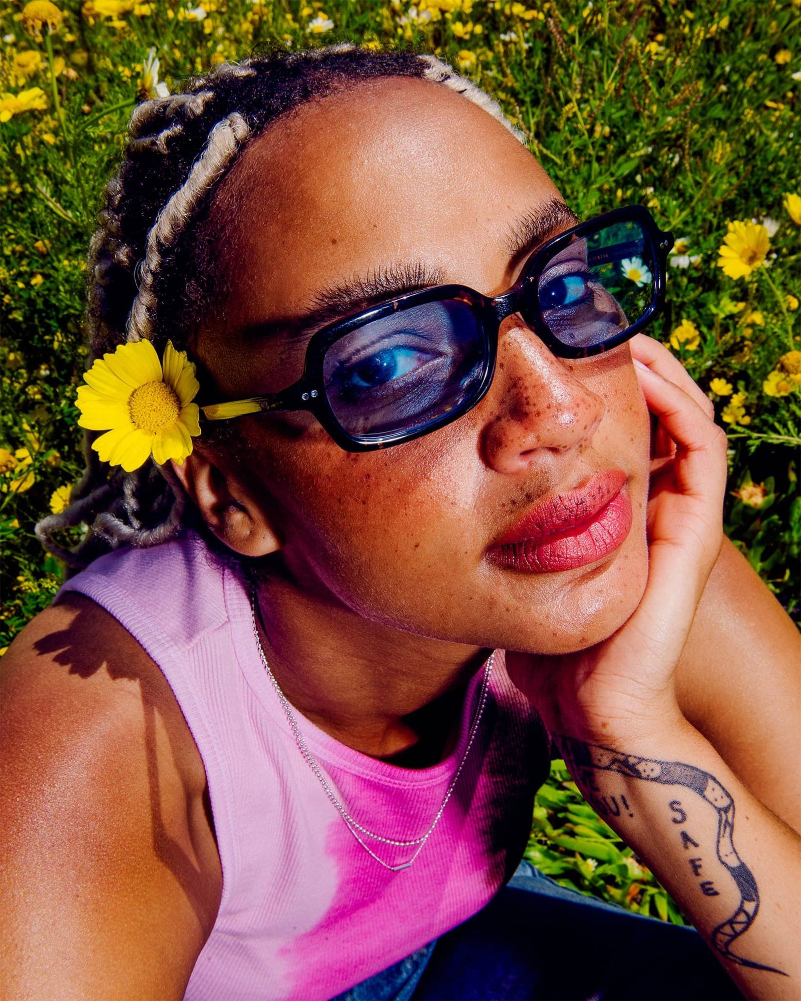 Person with sunglasses and a yellow flower in hair surrounded by flowers
