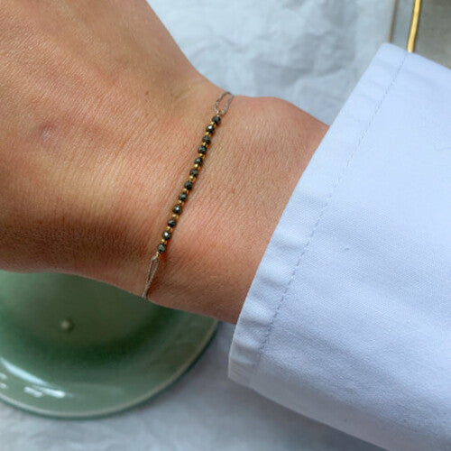 Delicate beaded bracelet with black and gold beads on thin chain worn on wrist against white sleeve