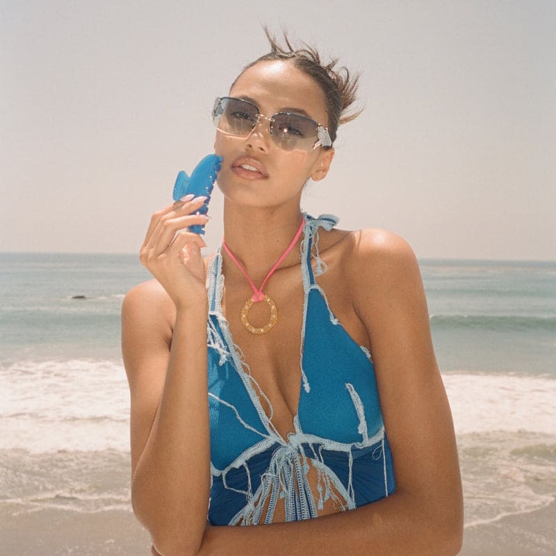 Woman wearing blue halter bikini top with tie-front detail and clear frame sunglasses at the beach