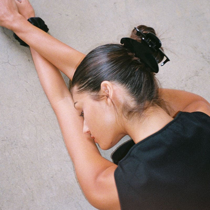 Black velvet scrunchie worn in hair, shown on model with messy bun hairstyle against neutral background