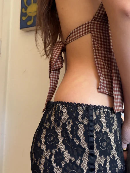Person wearing a checkered top and lace skirt with a neutral background