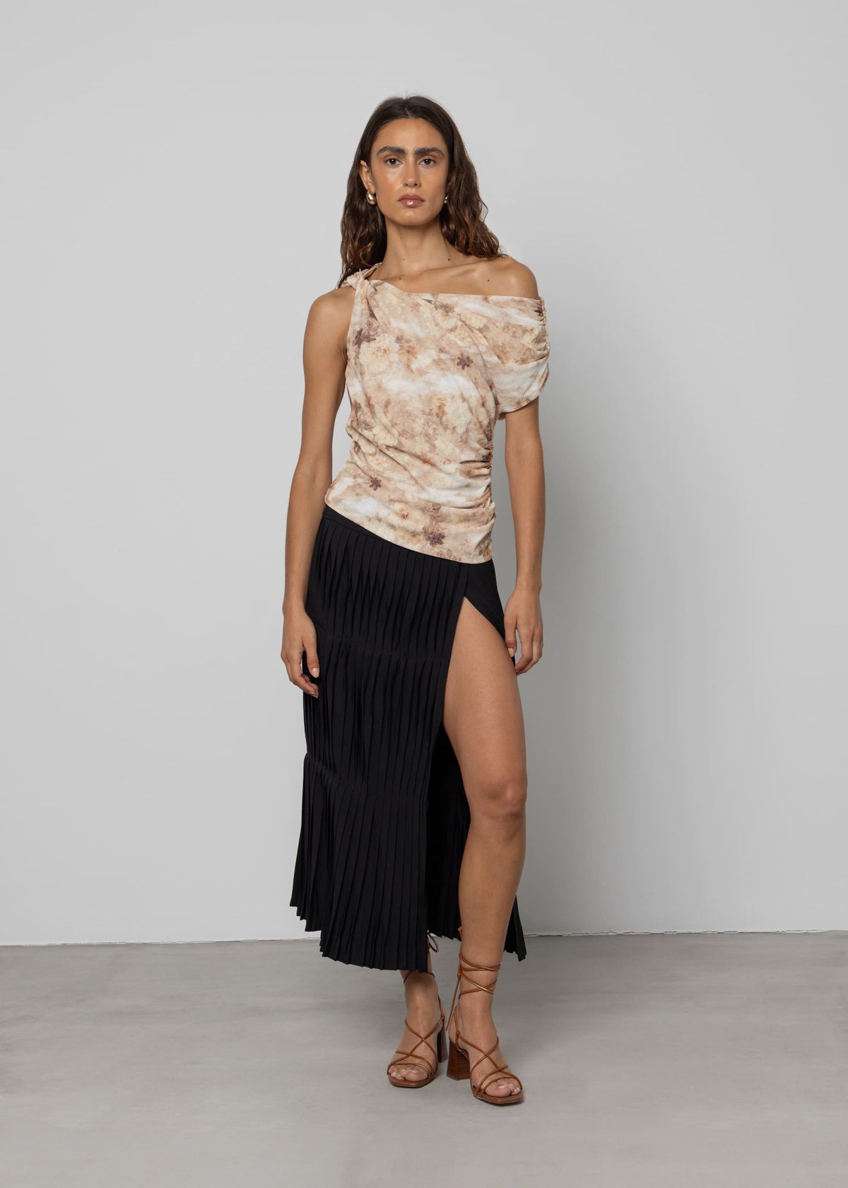 Black pleated midi skirt with high side slit, flowing fabric, shown with off-shoulder floral top and strappy heels.