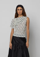 White and black polka dot asymmetric ruched top with one short sleeve and draped neckline detail.