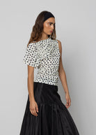 White polka dot ruched one-shoulder top with ruffled detail, paired with a black satin maxi skirt.