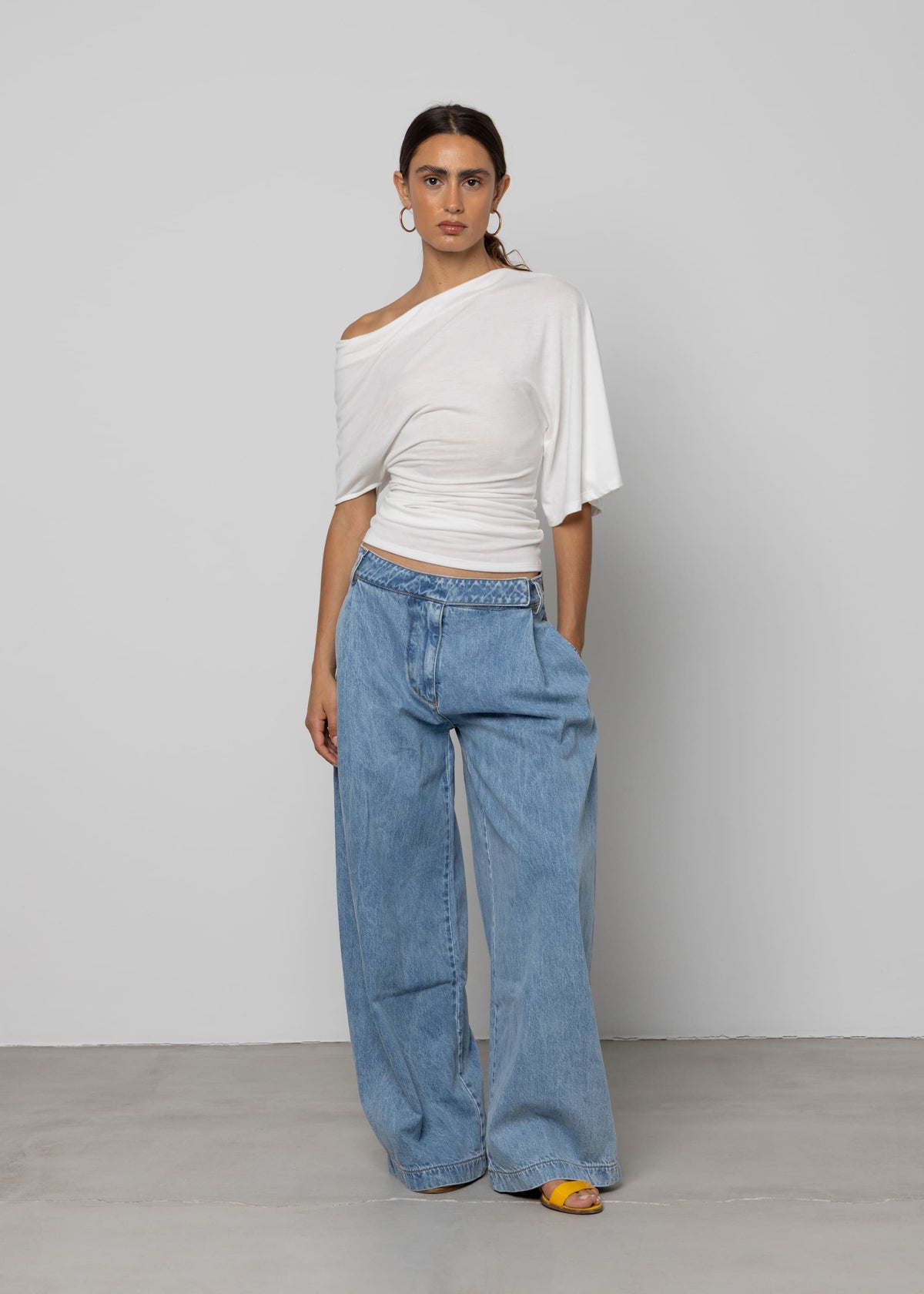 Wide-leg light wash blue denim jeans with pleated front, folded waistband detail, and relaxed silhouette.