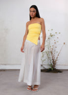 Yellow ruched strapless tube top with asymmetric hem, worn with white maxi skirt and white heeled sandals.