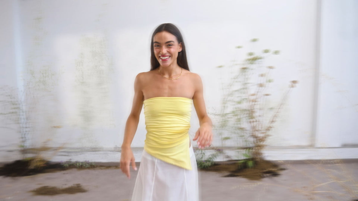 Yellow ruched strapless tube top with asymmetric hem, worn with white midi skirt and gold chain necklace.