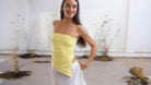 Yellow strapless ruched tube top with asymmetric hem, styled with white wide-leg pants and gold chain necklace.