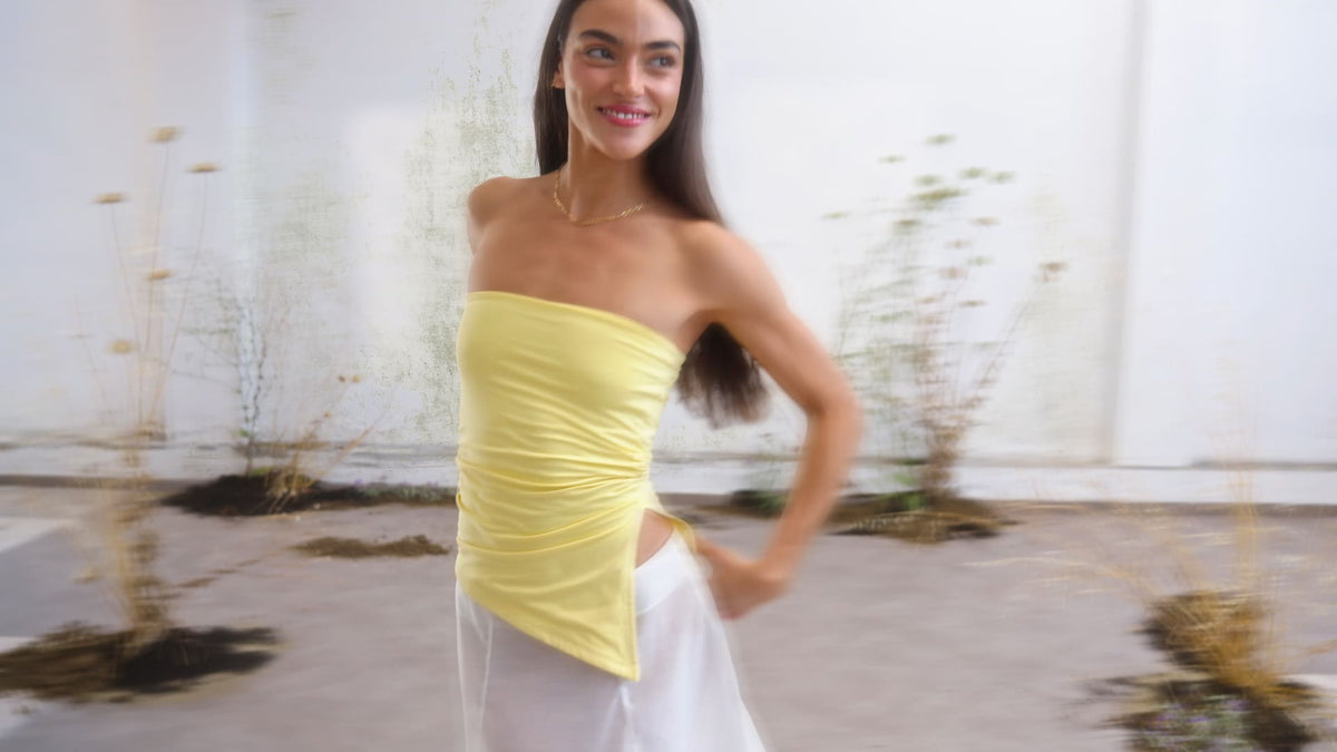 Yellow strapless ruched tube top with asymmetric hem, styled with white wide-leg pants and gold chain necklace.