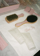 Pink and wood hair brush set with natural bristles displayed on white towel with beauty products and personalized storage case