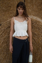 White ruched cotton crop top with thin straps and peplum hem, paired with navy wrap skirt against hay bale backdrop
