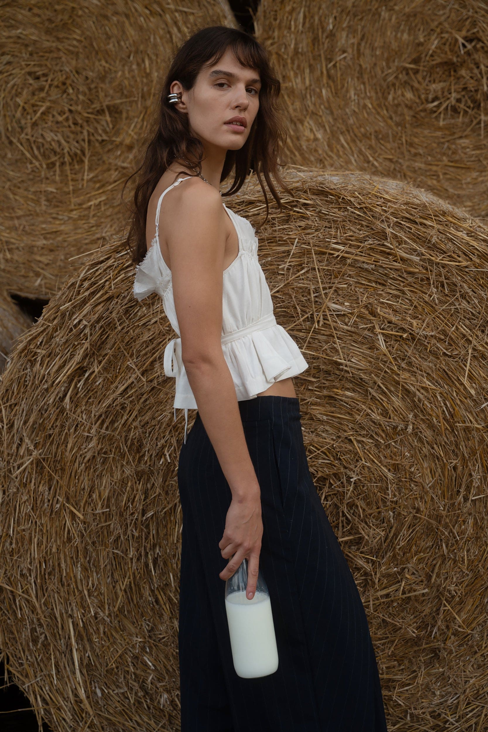 Woman in a white top and black skirt standing next to hay bales.