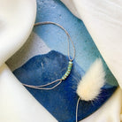 Delicate gold bracelet with green beads on watercolor blue ceramic dish with white fur accent