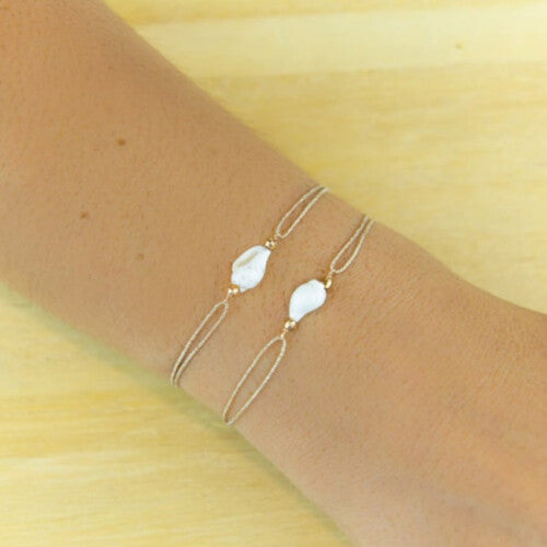 Delicate gold chain bracelet with white freshwater pearl centerpiece on wrist against wood background